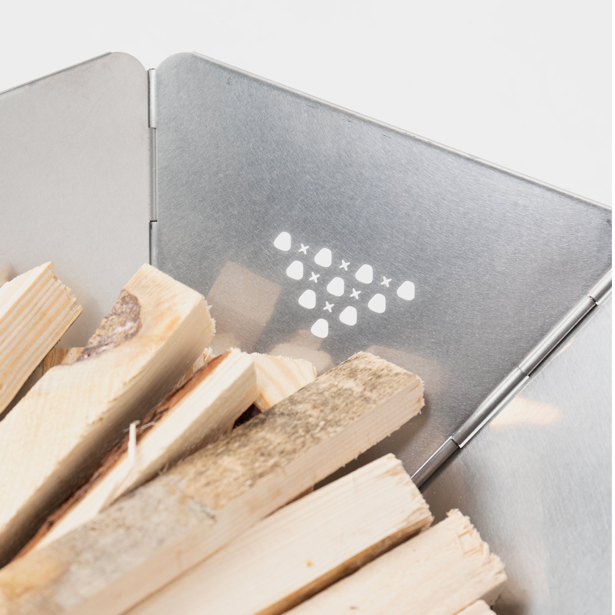 Stapel von Holzstücken in einem metallischen Behälter mit durchbrochenem Muster auf der Rückwand.