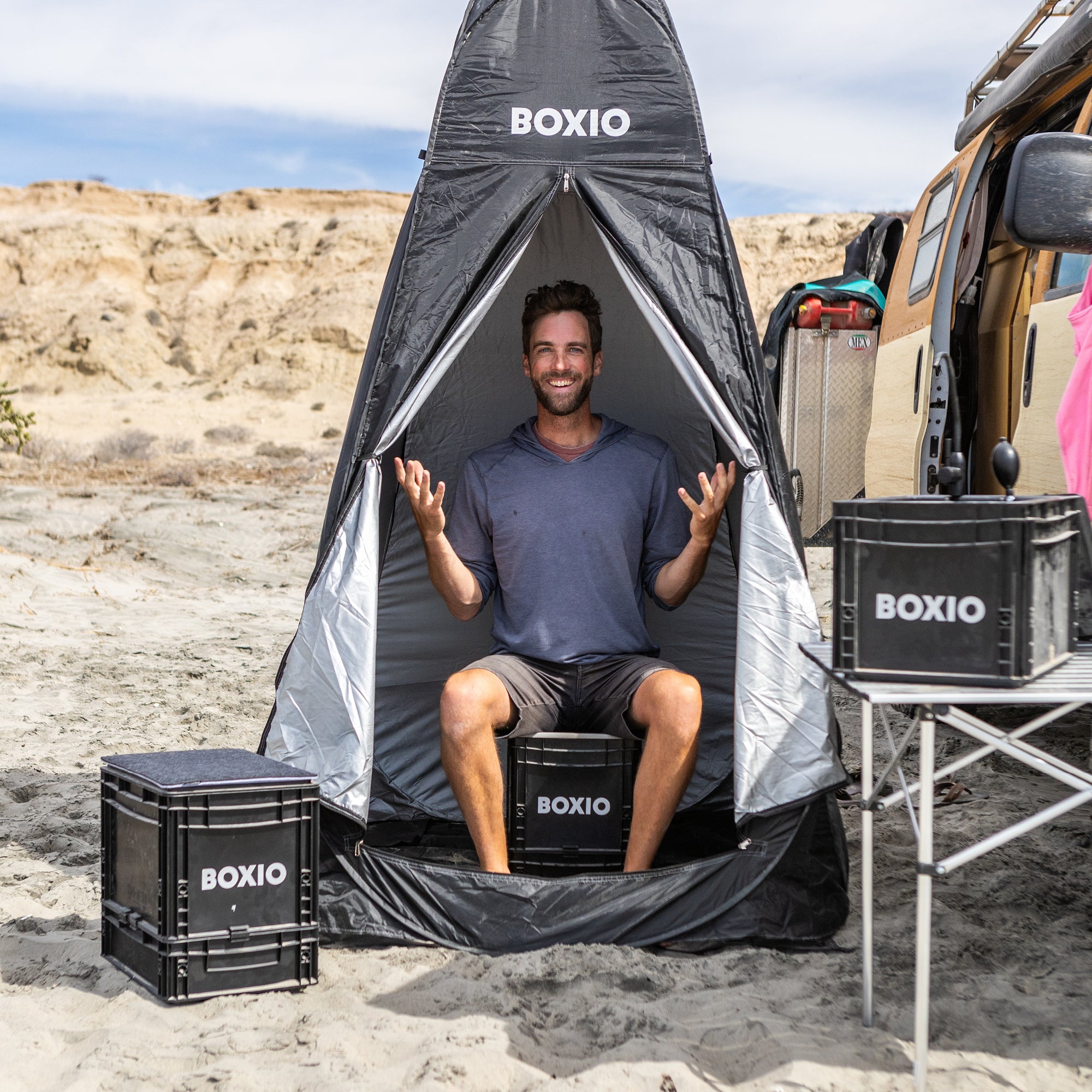 Man enjoying a portable BOXIO bathroom tent on the beach, featuring compact Eurobox design for outdoor convenience.