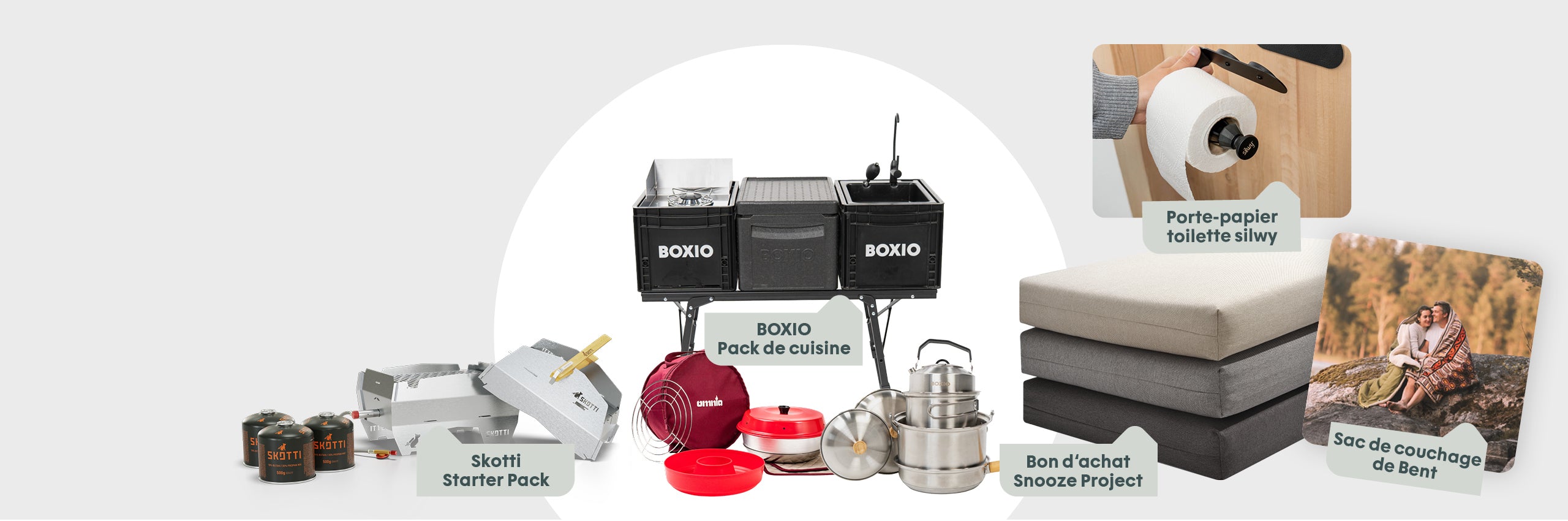 Koch- und Campingzubehör auf einem Tisch: BOXIO Küchenset, Skotti Starter Pack, Isolierbehälter, Campingmatten und Pärchen im Schlafsack.