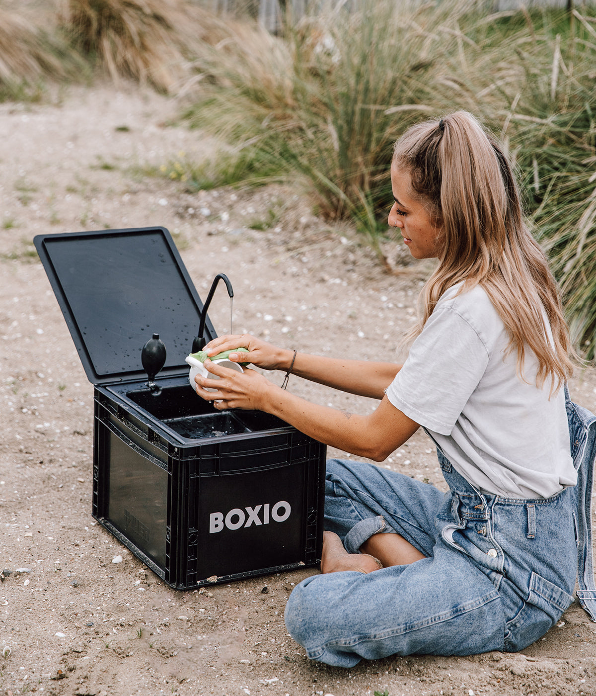 Frau wäscht mit mobilem Waschbecken am Strand eine Tasse ab 